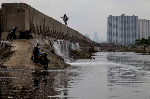 Pemancing  berjalan di atas tanggul laut raksasa yang bocor di Muara Baru, Jakarta, Sabtu (06/12/2025).
