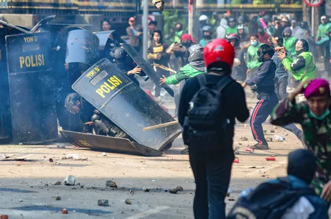 Anggota Brimob terjatuh saat massa melempar batu ke arah pasukan Brimob di Mako Brimob, Kwitang, jakarta, Jumat (29/08/2025).