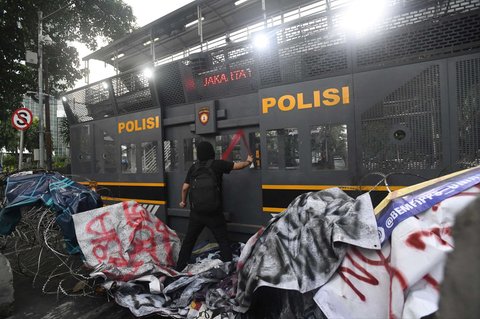 Seorang massa aksi tampak mencoreti barikade polisi selama demo 'Indonesia Gelap' di kawasan Patung Kuda, Jakarta, Kamis (20/2/2025).