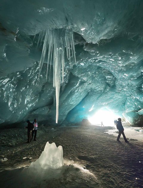 Pendaki berjalan dalam gua es yang terbentuk oleh air saat musim panas pada gletser Morteratsch yang  mencair akibat perubahan iklim di Pegunungan Alpen, Swiss, Sabtu (21/02/ 2025) waktu setempat.