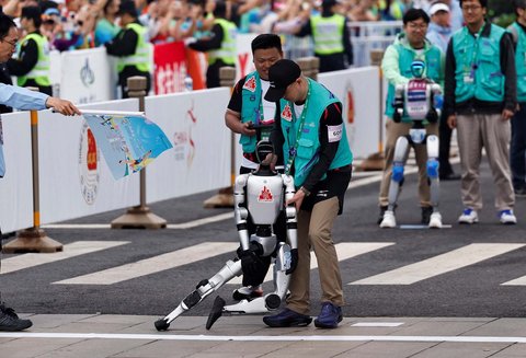 Teknisi memegang robot humanoid yang terjatuh di garis saat lomba lari setengah maraton robot humanoid di Beijing,  China,  (19/04/2025).