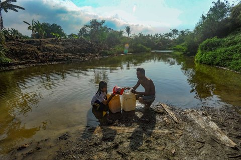 Seorang anak ditemani ayahnya mengambil air dari Kali Cihoe di Desa Sukagalih, Jonggol, Bogor, setelah berbulan-bulan dilanda krisis air bersih, Minggu (8/9/2024).