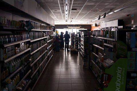 Pramuniaga berdiri di dalam swalayan tanpa lampu selama pemadaman listrik besar-besaran di Burgos, Spanyol, pada 28 April 2025.