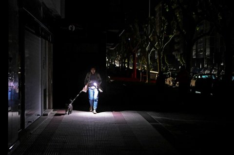 Seorang wanita menggunakan senter ponselnya saat melewati jalanan gelap gulita selama pemadaman listrik besar-besaran di Vigo, Spanyol, pada 28 April 2025.