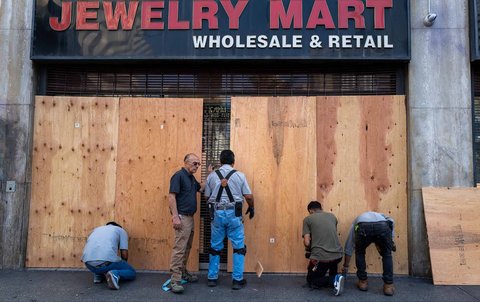 Para pekerja memasang papan kayu lapis  sebagai langkah pengamanan toko dari para penjarah di  pusat kota Los Angeles, Amerika Serikat, (10/06/2025)