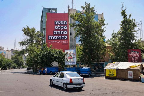 Poster anti-Israel dalam  bahasa Persia yang diterjemahkan "cari tempat berlindung di antara puing-puing", tergantung di sisi gedung di Teheran, Sabtu (14/06/2025).