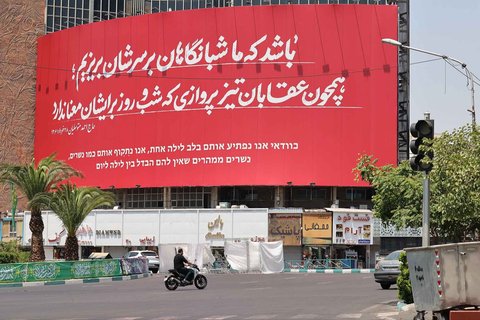 Seorang pria mengendarai sepeda motornya di samping poster anti-Israel di Teheran, Sabtu (14/06/2025).