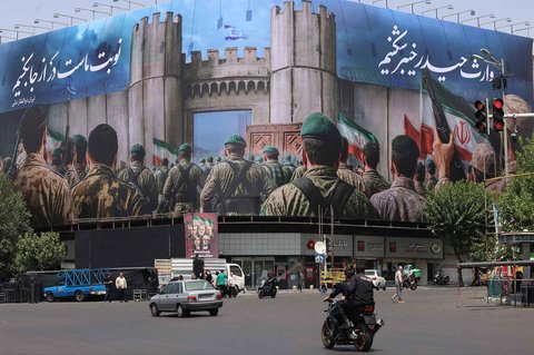 Seorang pria mengendarai sepeda motornya di samping poster anti-Israel di Teheran, Sabtu (14/06/2025).