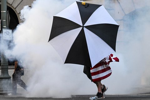 Seorang pengunjuk rasa memegang payung saat berjalan di tengah gas air mata saat aksi  menentang Presiden AS Donald Trump di Los Angeles, California, AS, Sabtu (14/06/2025) waktu setempat.