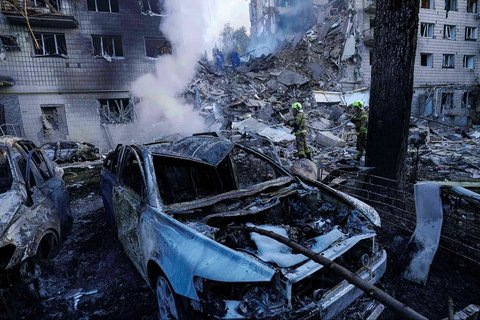 Petugas penyelamat memadamkan api di sebuah mobil di depan sebuah rumah tinggal bertingkat yang hancur akibat serangan Rusia di Kyiv, Ukraina, Selasa, (17/06/2025).