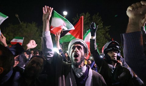Para pengunjuk rasa mengibarkan bendera Iran dan bendera Palestina saat mereka berkumpul di depan Kedutaan Besar Inggris di Teheran pada tanggal 14 April 2024. (ATTA KENARE/AFP)