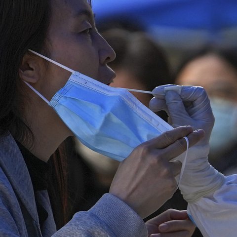 Seorang perempuan memegang maskernya saat tes usap selama pengujian COVID-19 publik di distrik Chaoyang, Beijing, Rabu (11/5/2022). Shanghai pada Rabu menegaskan kembali akan mempertahankan pendekatan &ldquo;nol-COVID&rdquo; pengendalian pandemi, sehari setelah kepala Organisasi Kesehatan Dunia (WHO) menyatakan kebijakan itu tidak berkelanjutan dan mendesak China mengubah strategi. (AP Photo/Andy Wong)
