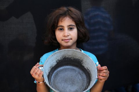 Seorang anak  Palestina memegang panci kosong sambil menunggu di titik distribusi makanan hangat di Nuseirat di Jalur Gaza bagian tengah, (04/06/2025)