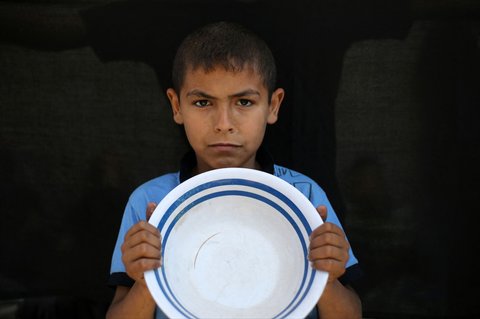 Seorang anak  Palestina memegang panci kosong sambil menunggu di titik distribusi makanan hangat di Nuseirat di Jalur Gaza bagian tengah, (04/06/2025)