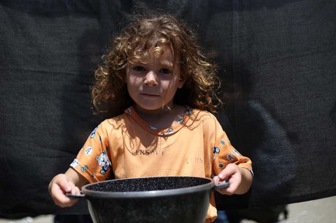 Seorang anak  Palestina memegang panci kosong sambil menunggu di titik distribusi makanan hangat di Nuseirat di Jalur Gaza bagian tengah, (04/06/2025)