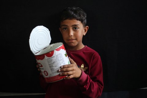 Seorang anak  Palestina memegang panci kosong sambil menunggu di titik distribusi makanan hangat di Nuseirat di Jalur Gaza bagian tengah, (04/06/2025)