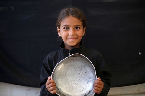 Seorang anak  Palestina memegang panci kosong sambil menunggu di titik distribusi makanan hangat di Nuseirat di Jalur Gaza bagian tengah, (04/06/2025)
