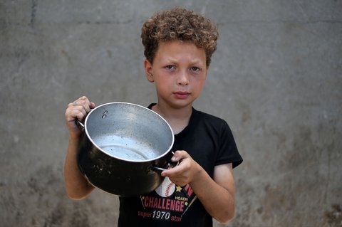 Seorang anak  Palestina memegang panci kosong sambil menunggu di titik distribusi makanan hangat di Nuseirat di Jalur Gaza bagian tengah, (04/06/2025)