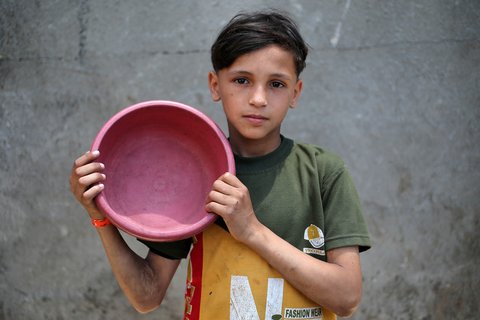 Seorang anak  Palestina memegang panci kosong sambil menunggu di titik distribusi makanan hangat di Nuseirat di Jalur Gaza bagian tengah, (04/06/2025)