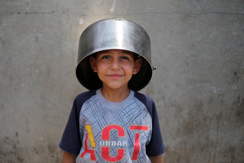 Seorang anak Palestina menutupi kepalanya dengan panci  kosong saat menunggu di titik distribusi makanan hangat di Nuseirat di Jalur Gaza bagian tengah, (04/06/2025).