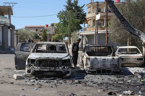 Seorang anggota pasukan keamanan Suriah melihat kendaraan-kendaraan yang terbakar di tengah bentrokan antara pejuang Druze dan suku Badui di kota Suwayda, Suriah, Rabu (16.07/2025).