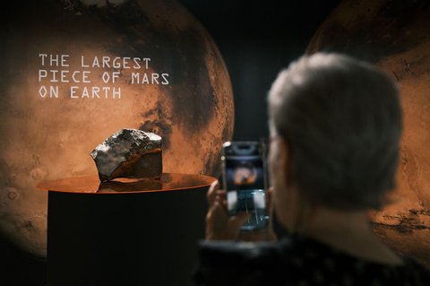 Seorang perempuan mengambil foto meteorit Mars seberat 22,5 kg NWA 16788 yang dipamerkan dalam pratinjau lelang Sotheby's di New York, AS, (15/07/2025).