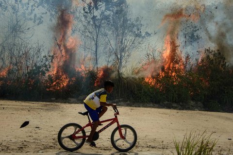 Warga mengendarai sepeda melewati kebakaran hutan di Karya Indah, Provinsi Riau, Sabtu (19/07/2025).