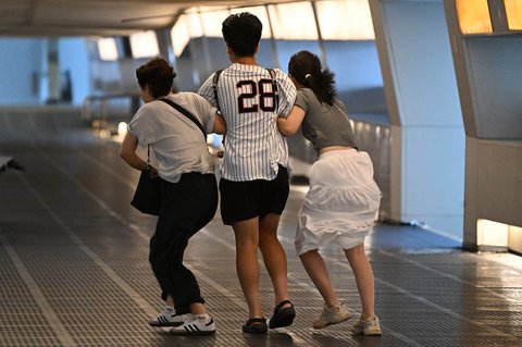 Warga berjalan di tengah angin kencang di Distrik Central, Hong Kong, Minggu (20/07/2025).