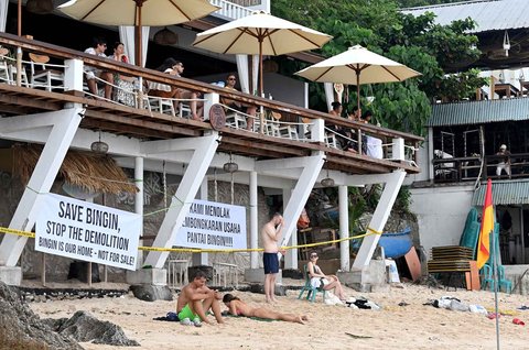 Wisatawan beraktivitas di depan restoran yang dibongkar di Pantai Bingin, Desa Pecatu, Kabupaten Badung, Bali, Rabu (23/07/2025).