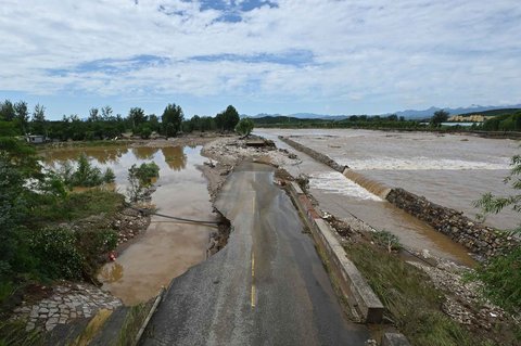 Jalan yang rusak akibat banjir di sepanjang sungai yang meluap di  Distrik Miyun, pinggiran Beijing,  China, Selasa (29/07/2025).