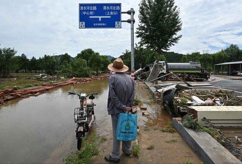 Seorang pria berdiri di samping jalan yang tergenang air dan dipenuhi puing-puing akibat banjir di Distrik Miyun, pinggiran Beijing, China, Selasa (29/07/2025).
