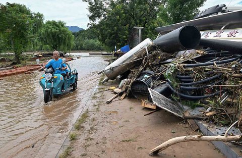 Warga mengendarai kendaraannya melewati puing-puing di sepanjang jalan yang terendam banjir di Distrik Miyun, pinggiran Beijing, China, Selasa (29/07/2025).