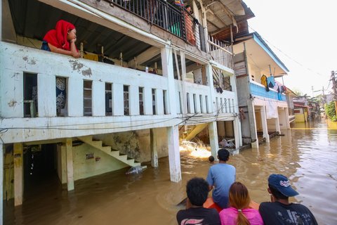 Warga beraktifitas saat banjir merendam pemukiman di Jalan Pirus, Kelurahan Bidara Cina, Jatinegara, Jakarta Timur, Minggu (06/07/2025).