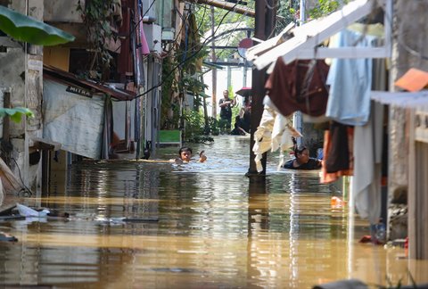 Warga beraktifitas saat banjir merendam pemukiman di Jalan Pirus, Kelurahan Bidara Cina, Jatinegara, Jakarta Timur, Minggu (06/07/2025).