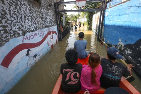Warga beraktifitas saat banjir merendam pemukiman di Jalan Pirus, Kelurahan Bidara Cina, Jatinegara, Jakarta Timur, Minggu (06/07/2025).