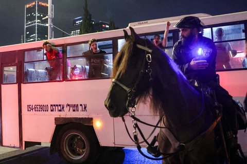 Seorang polisi Israel yang berkuda mengawasi para demonstran yang ditahan meneriakkan slogan-slogan dari dalam bus polisi menyusul demonstrasi yang diselenggarakan oleh keluarga para sandera Israel yang ditawan di Jalur Gaza di luar kantor pusat Kementerian Pertahanan di Tel Aviv, Israel, Sabtu (09/08/2025) malam.