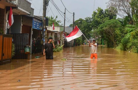 Warga  mencopot bendera merah putih yang dipasang depan rumahnya saat banjir  merendam kawasan Perumahan Villa Pamulang, Kelurahan Pondok Petir, Kecamatan Bojongsari, Kota Depok, Jawa Barat, Minggu (10/8/2025).