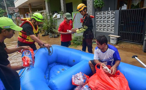 Relawan  membagikan nasi bungkus kepada warga menggunakan perahu karet setelah banjir  merendam kawasan Perumahan Villa Pamulang, Kelurahan Pondok Petir, Kecamatan Bojongsari, Kota Depok, Jawa Barat, Minggu (10/8/2025).