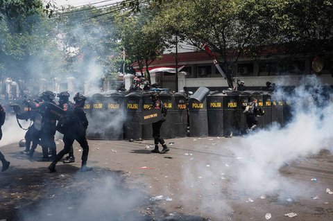 Petugas polisi berlindung sambil melepaskan gas air mata saat aksi ribuan warga  di depan Kantor Bupati Pati, Jawa Tengah. Rabu (13/08/2025).