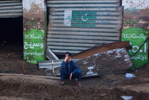 Seorang anak laki-laki duduk di depan toko-toko yang rusak akibat banjir bandang di pinggiran Pir Baba, distrik Buner, di barat laut Pakistan,  Sabtu (16/08/2025