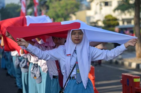 Ribuan pelajar dari berbagai sekolah di Surabaya membentangkan bendera merah putih sepanjang 14. 905 meter di di Jalan Gubernur Suryo Surabaya, Minggu (17/08/2025).