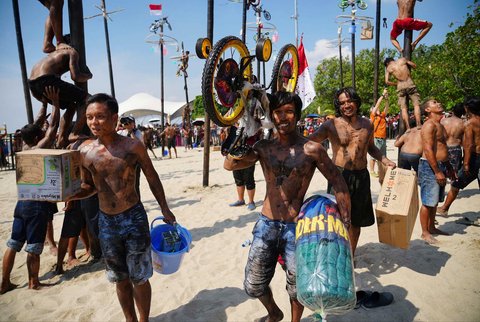 Peserta membawa hadiah usai berhasil memanjat batang pinang saat perlombaan memperingati Kemerdekaan RI di Beach Pool, Ancol Jakarta, Minggu (17/8/2025).