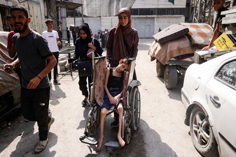 Seorang perempuan Palestina mendorong kursi roda anaknya saat mengungsi bersama warga lain dari permukiman Abu Iskandar di utara Kota Gaza, Palestina, Jumat (22/08/2025).