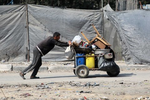 Seorang pria Palestina mendorong gerobak penuh barang-barang rumah tangga saat ia mengungsi dari permukiman Abu Iskandar di utara Kota Gaza,  Palestina, Jumat (22/08/2025).