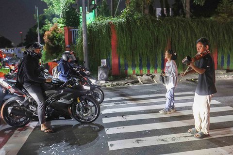 Pengamen Kris Violist dan istrinya saat memainkan musik biola di perempatan Juanda, Depok, Jumat malam (22/08/2025).