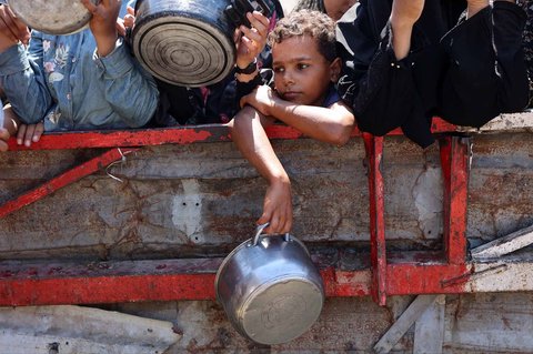 Seorang anak Palestina memegang panci kosong sambil menunggu nasi matang di depan dapur amal di Kota Gaza, Sabtu (23/08/2025).