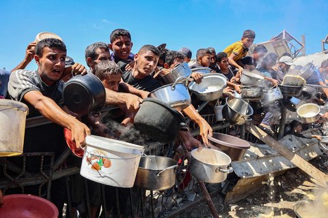 Warga Palestina mengulurkan panci kosong mereka untuk menerima nasi dari dapur amal di Kota Gaza, Sabtu (23/08/2025).