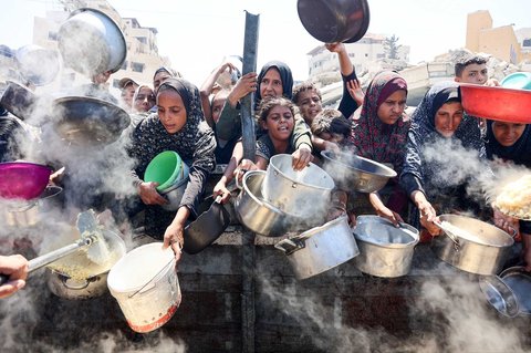 Warga Palestina mengulurkan panci kosong mereka untuk menerima nasi dari dapur amal di Kota Gaza, Sabtu (23/08/2025).