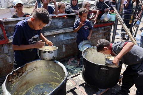 Anak-anak Palestina mengeruk dasar panci besar untuk mengambil sisa nasi yang sudah  dibagikan di dapur umum di Kota Gaza,  Sabtu (23/08/2025).