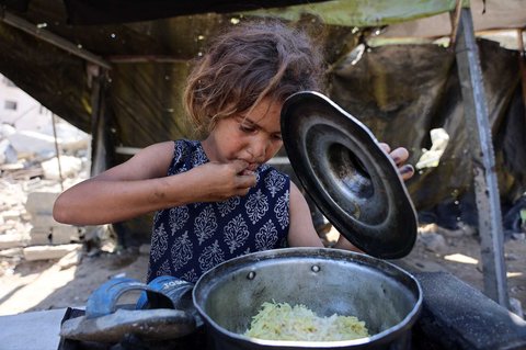 Seorang anak Palestina memakan nasi yang sudah dimasak dengan tangannya setelah menerimanya dari dapur amal di Kota Gaza Sabtu (23/08/2025).
